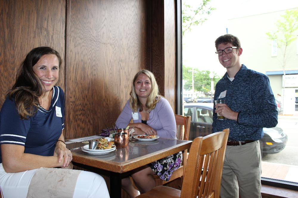 three alumni sitting at a table and smiling for camera